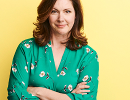 A middle-aged white woman with a slight smile and her arms crossed in front of her chest.