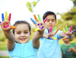Three young children playing outdoors with brightly painted hands. 