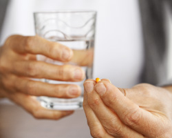 Person holding a glass of water and a pill in the other hand.