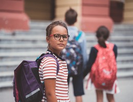 A girl with a backpack in front of her school steps