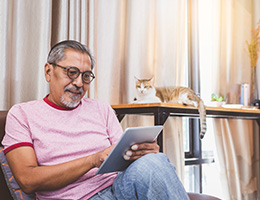 A senior man is sitting on a couch, looking at a computer tablet.