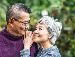 A woman rests her hands and cheek on a man's shoulder while looking up at him.