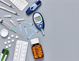 A photo of diabetes-related supplies, including packets of pills, a bottle of pills, needles, test strips and a meter for testing blood sugar levels.