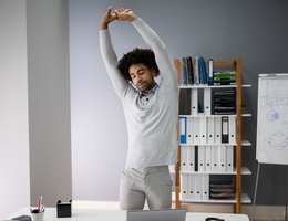 Man standing by his desk and stretching his arms above his head.