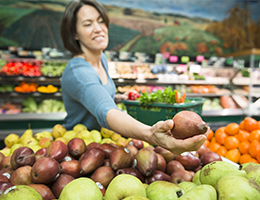 A woman shopping for sweet potatoes in a grocery store.