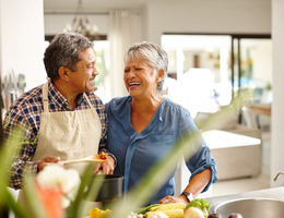 Man and woman laughing together while preparing fresh vegetable soup.