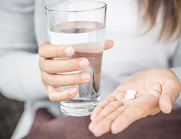 A pair of hands holding a glass of water and two white tablets.