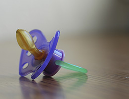 A green and purple pacifier sits on a smooth woodgrain surface. 