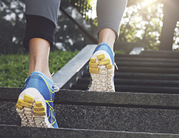 A pair of feet in blue, yellow and white running shoes, walking up a flight of concrete stairs. 