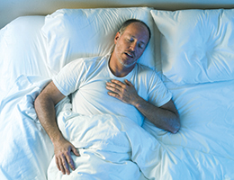   An open-mouthed man asleep in bed.