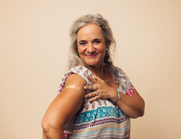 A smiling woman shows her flu vaccine bandage