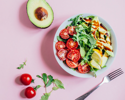 A summer salad in a bowl next to half an avocado.