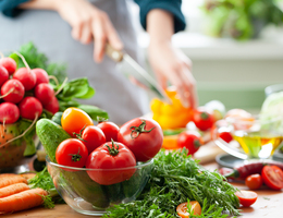 Photo of a person's hands chopping fresh vegetables with a knife.