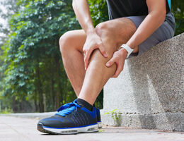 A person in exercise clothes clutches their achy leg.