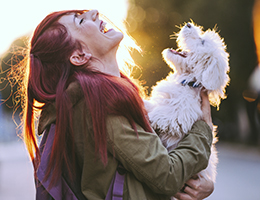 A woman laughs while holding a small dog.