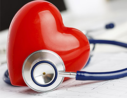 A blue stethoscope wraps around a shiny red plastic heart. 