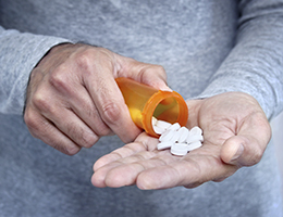 A man pours a prescription bottle of pills into his hand. 