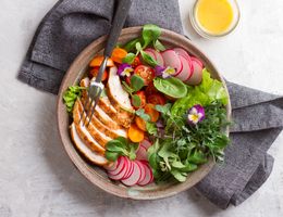 A plateful of salad with a small glass cup of lemon dressing on the side.