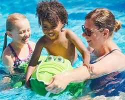  Two smiling kids and a smiling woman play in a pool.