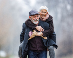  Two warmly-dressed seniors laugh outdoors.