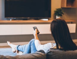 A woman with a remote control sitting in front of a TV.