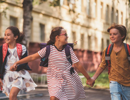 Three kids wearing backpacks walk while holding hands.