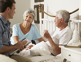 A healthcare worker visits a man and woman at home in bed.  