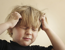 A young boy grimaces as he holds his head with both hands.