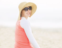  A smiling woman wearing a wide-brimmed hat, long sleeves and sunglasses.