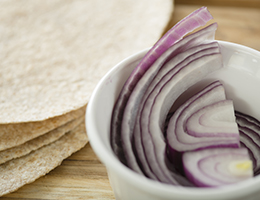 A ramekin with red onions next to a stack of tortillas.