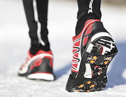 Close-up image of red, black and white running shoes as a person walks through the snow.