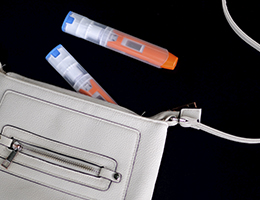 A white leather handbag with two EpiPens spilling out of it.