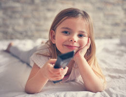 A young girl rests her chin in her hand and holds a TV remote in the other hand.
