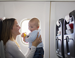 A mom holding a baby while seated on an airplane.