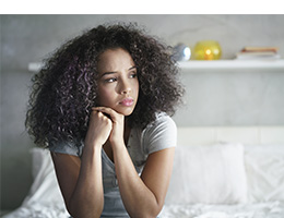 A teenage girl sitting on a bed looking sad.