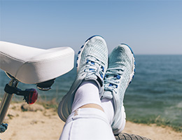 A pair of feet in athletic shoes resting next to a bicycle seat at the beach. 