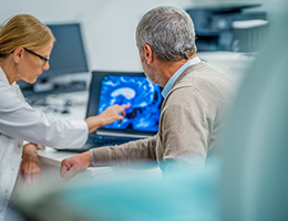 A female doctor is pointing to a brain scan while an older man looks at the scan.