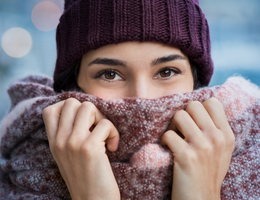 A woman in a hat holds a scarf over her face