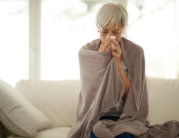 A woman wrapped in a blanket blows her nose.