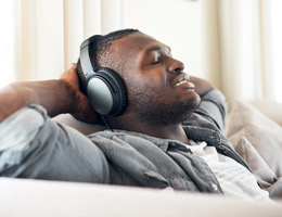 A relaxed man sitting on a couch with eyes closed and headphones on.